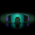 Oakley Hydra sunglasses with translucent frame and iridescent blue-green mirrored lenses on reflective surface