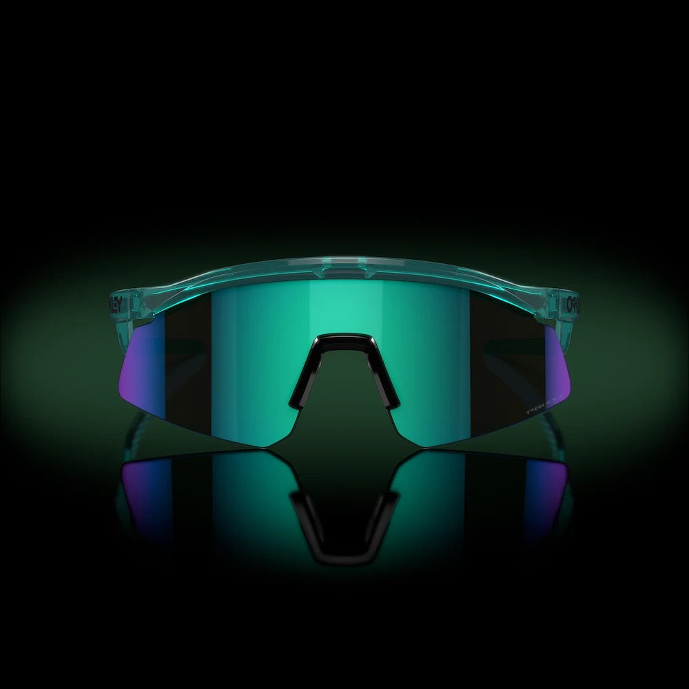 Oakley Hydra sunglasses with translucent frame and iridescent blue-green mirrored lenses on reflective surface