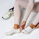 Person putting on white Feetures invisible running socks with athletic wear and sneakers