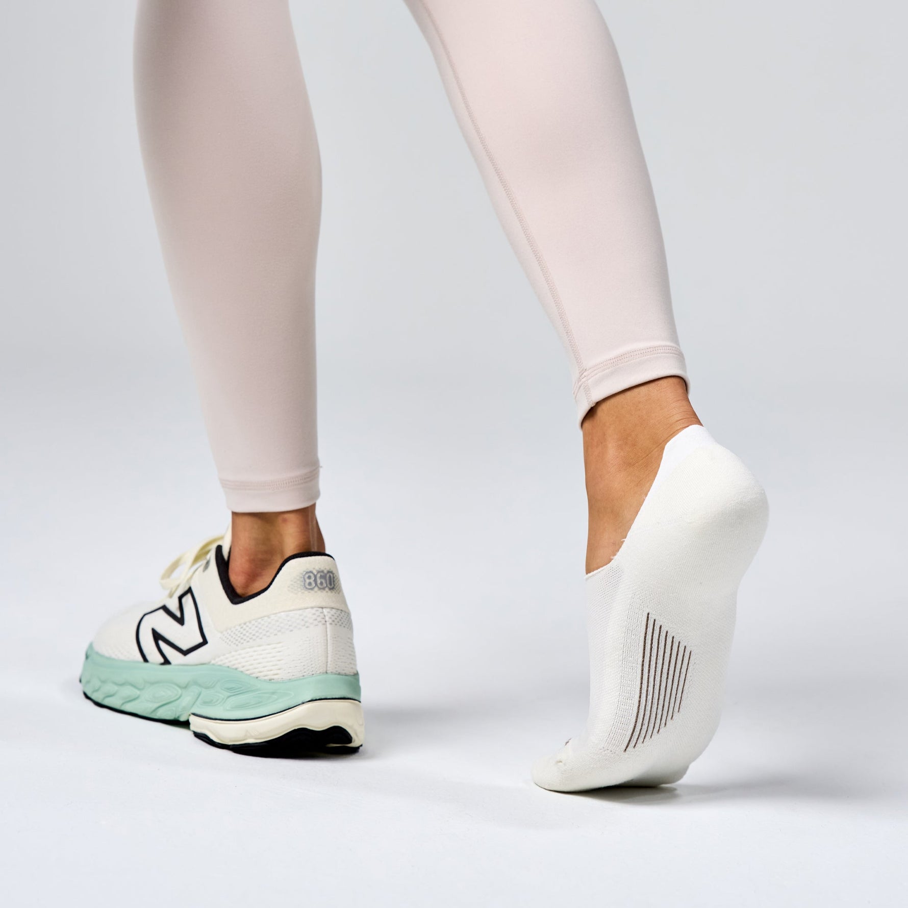 White Feetures Elite Light Cushion Invisible socks on model's feet with New Balance sneakers