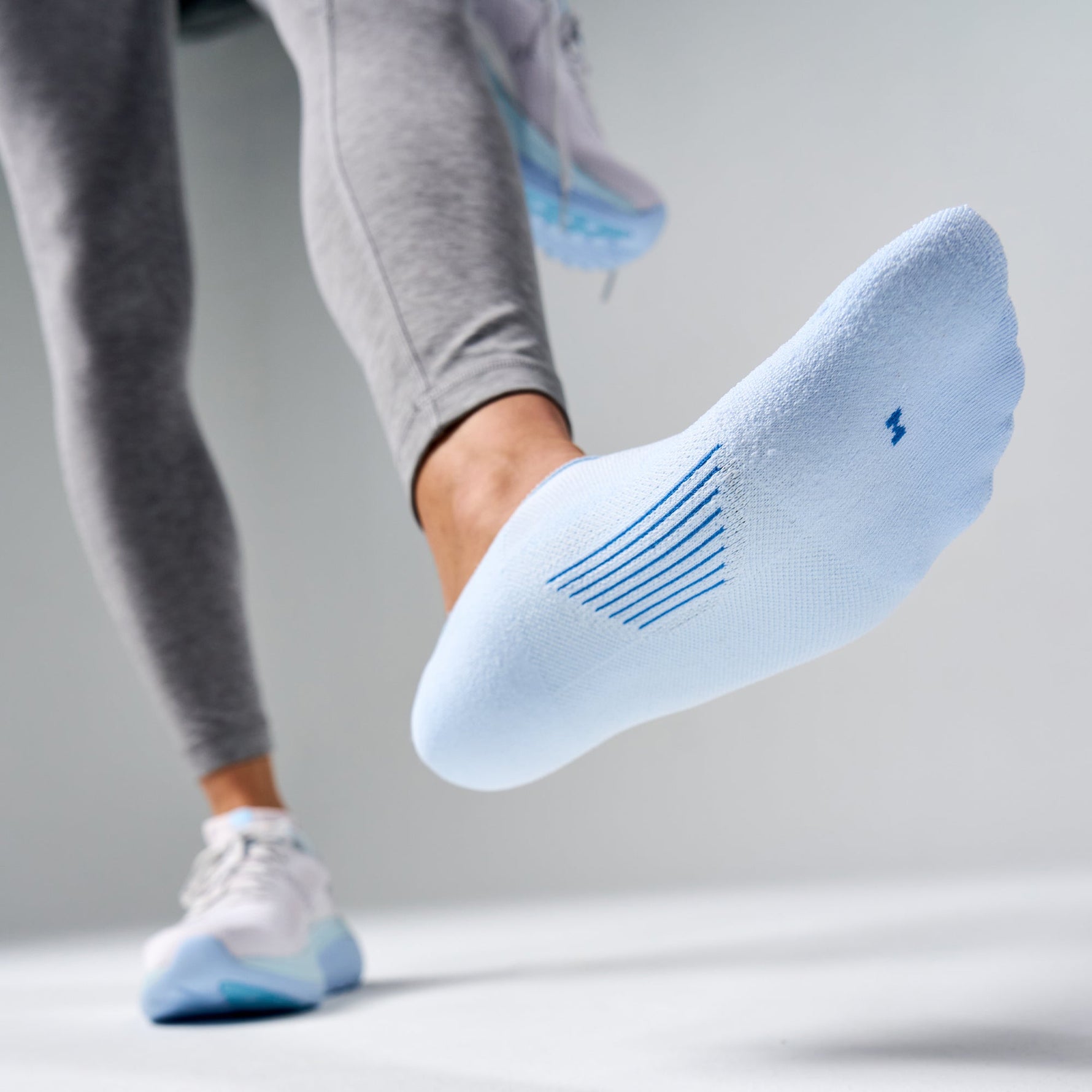 White Feetures Elite Light Cushion Invisible sock with blue stripes worn during exercise