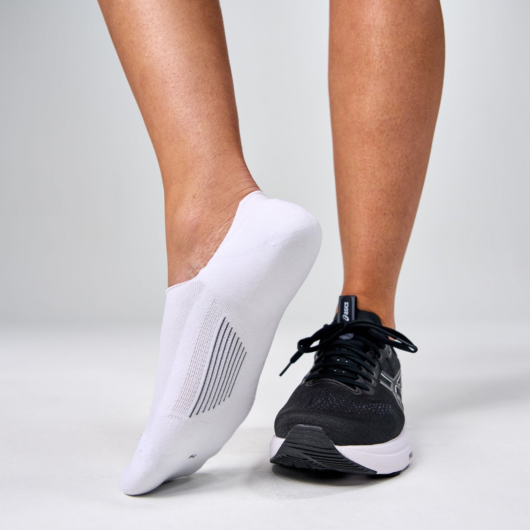 White Feetures Elite Light Cushion Invisible socks worn with black running shoes