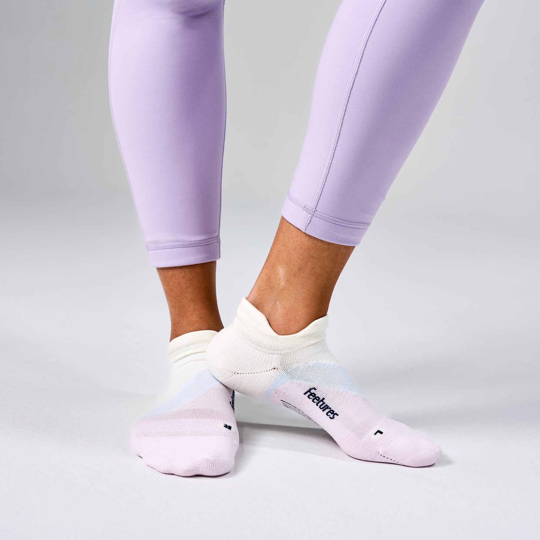 Feetures Elite Light Cushion Tab socks in white and pink gradient worn with purple leggings