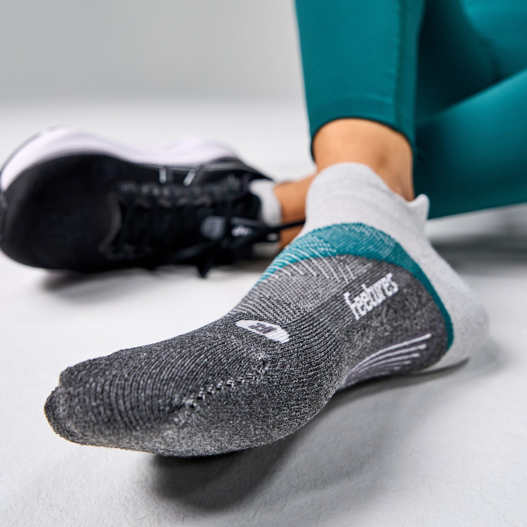 Feetures Elite Light Cushion Tab sock in grey with teal trim on foot