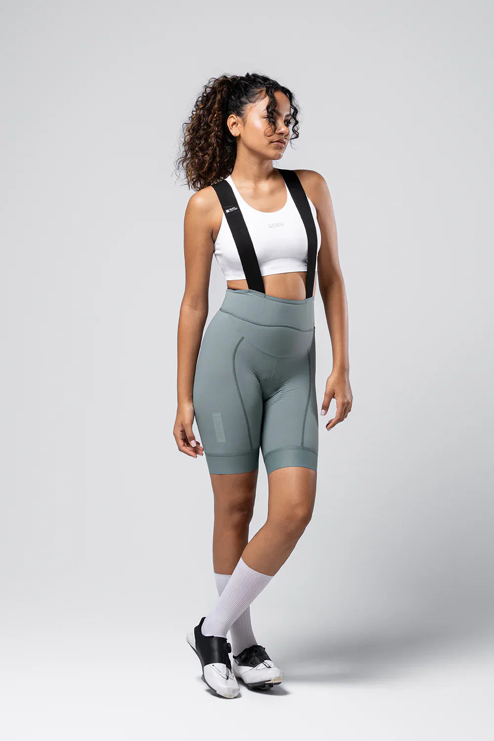 Woman wearing Gobik Matt 2.0 bib shorts in sage green with white sports bra