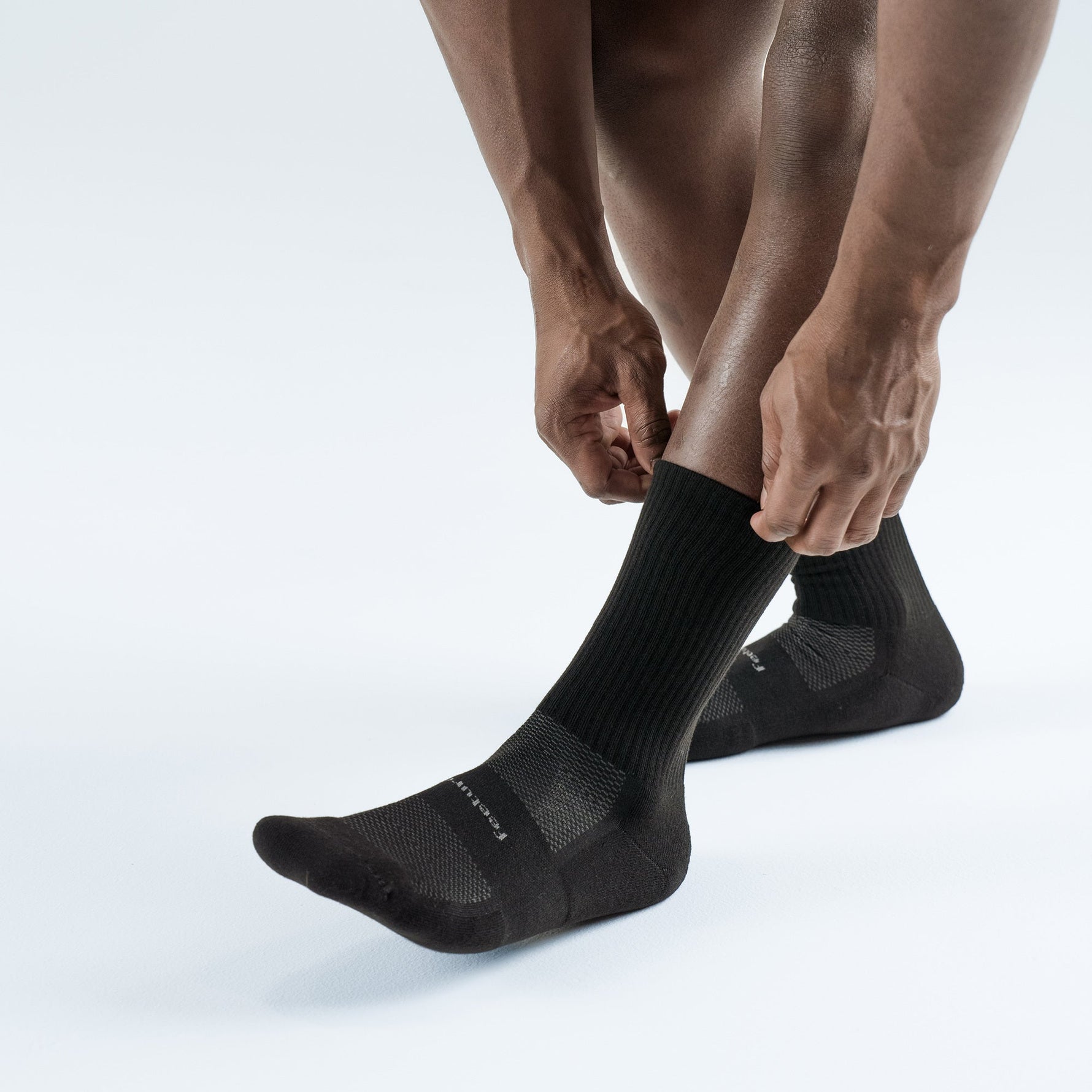 Person pulling on black Feetures High Performance Max Cushion Crew socks on both feet
