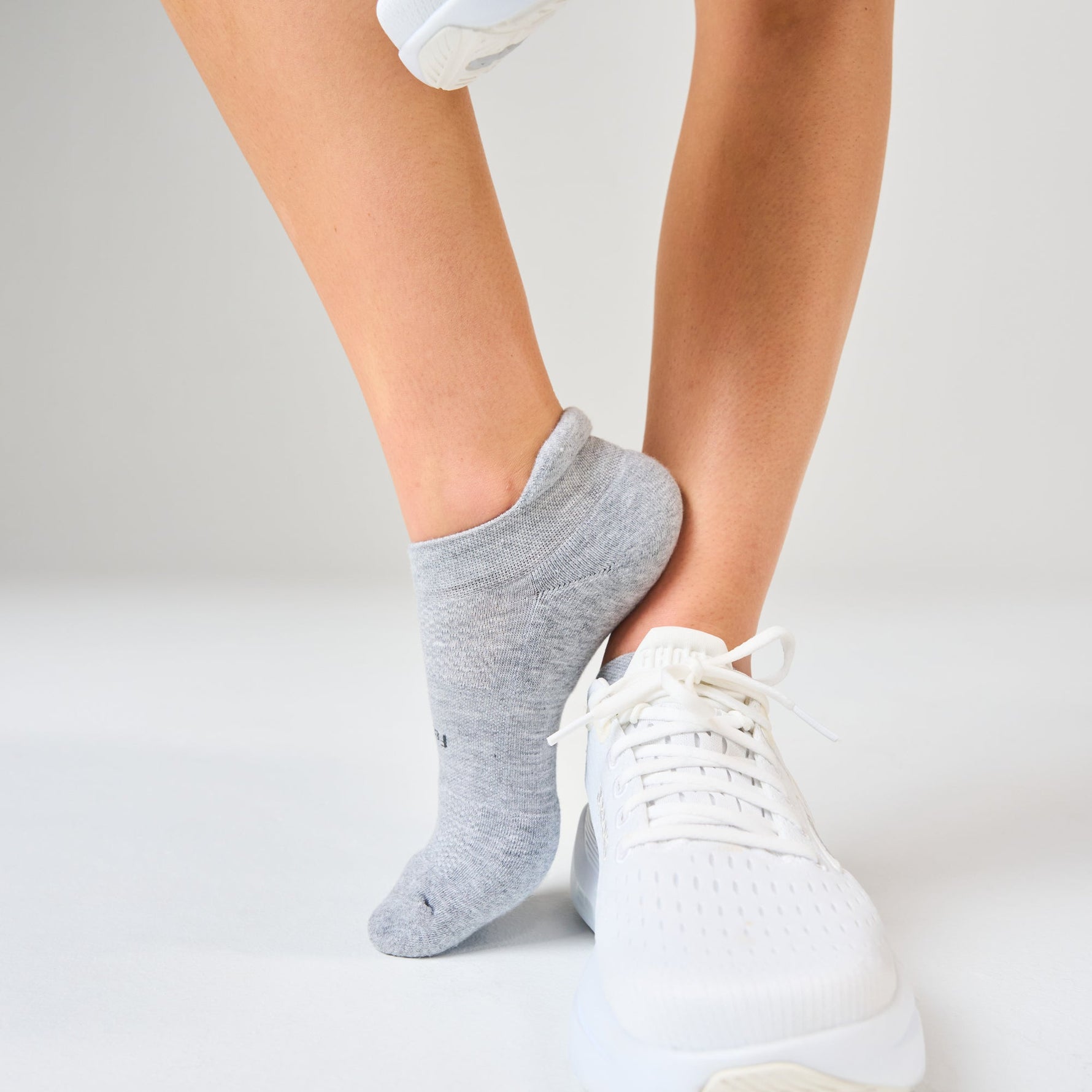 Person wearing heather grey Feetures no-show tab socks with white sneakers