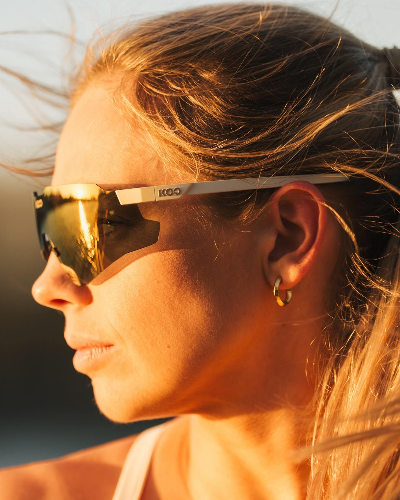 Woman wearing KOO Nebula sunglasses in Vanilla Matt Dark Gold Mirror finish in golden sunlight