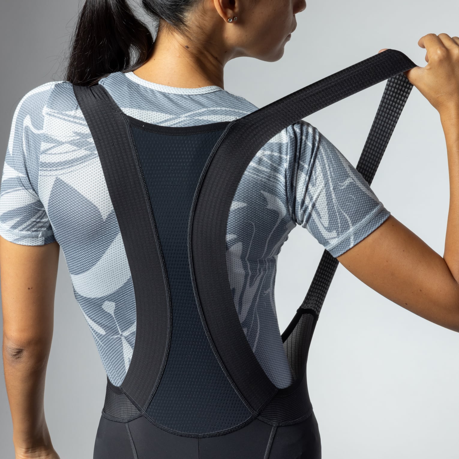 Woman wearing black cycling bibshorts with white patterned athletic top, professional studio lighting