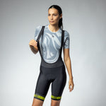 Woman wearing black ALE cycling bibshorts with yellow accents and gray patterned jersey