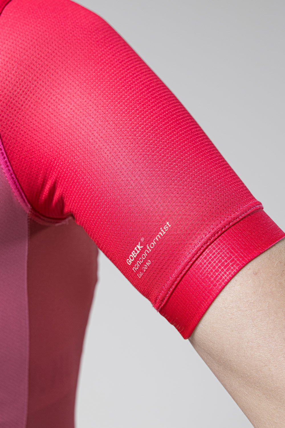 Close-up of bright pink Gobik cycling jersey sleeve showing textured fabric and brand logo