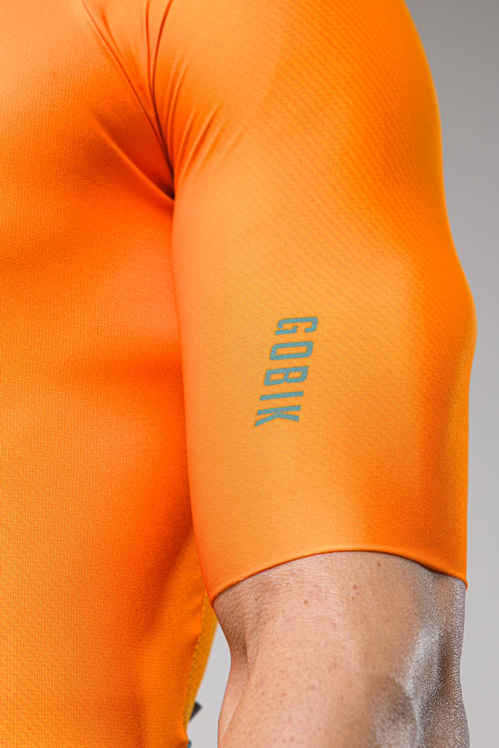 Close-up of orange Gobik cycling jersey sleeve showing brand text and technical fabric details
