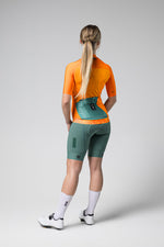 Back view of cyclist wearing orange Gobik CX Pro jersey with green shorts