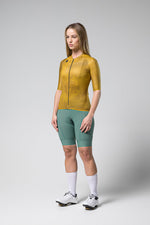 Woman wearing Gobik Infinity short sleeve cycling jersey in ginger yellow with green shorts