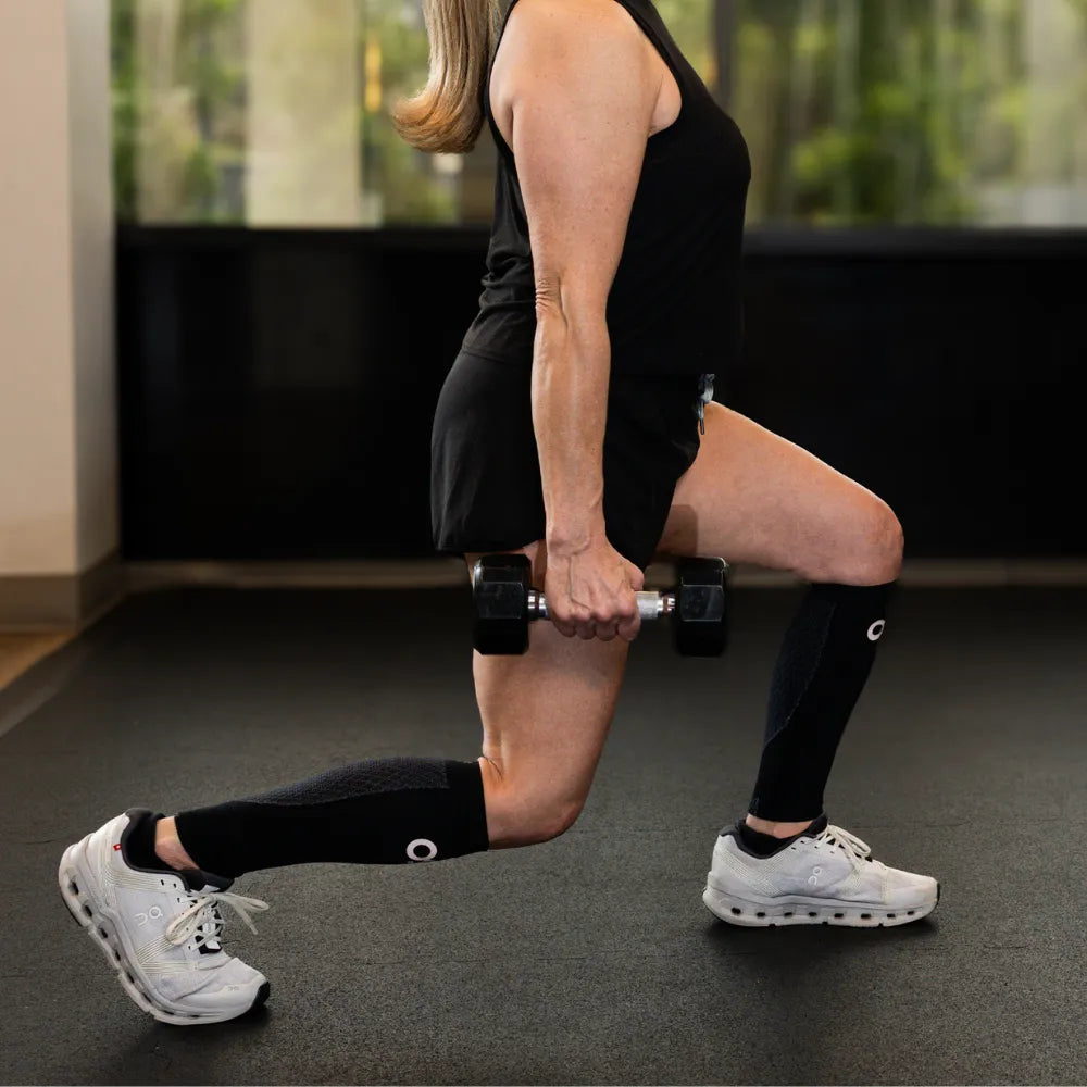 Woman wearing black OS1st CS6 performance calf sleeves while exercising with dumbbells
