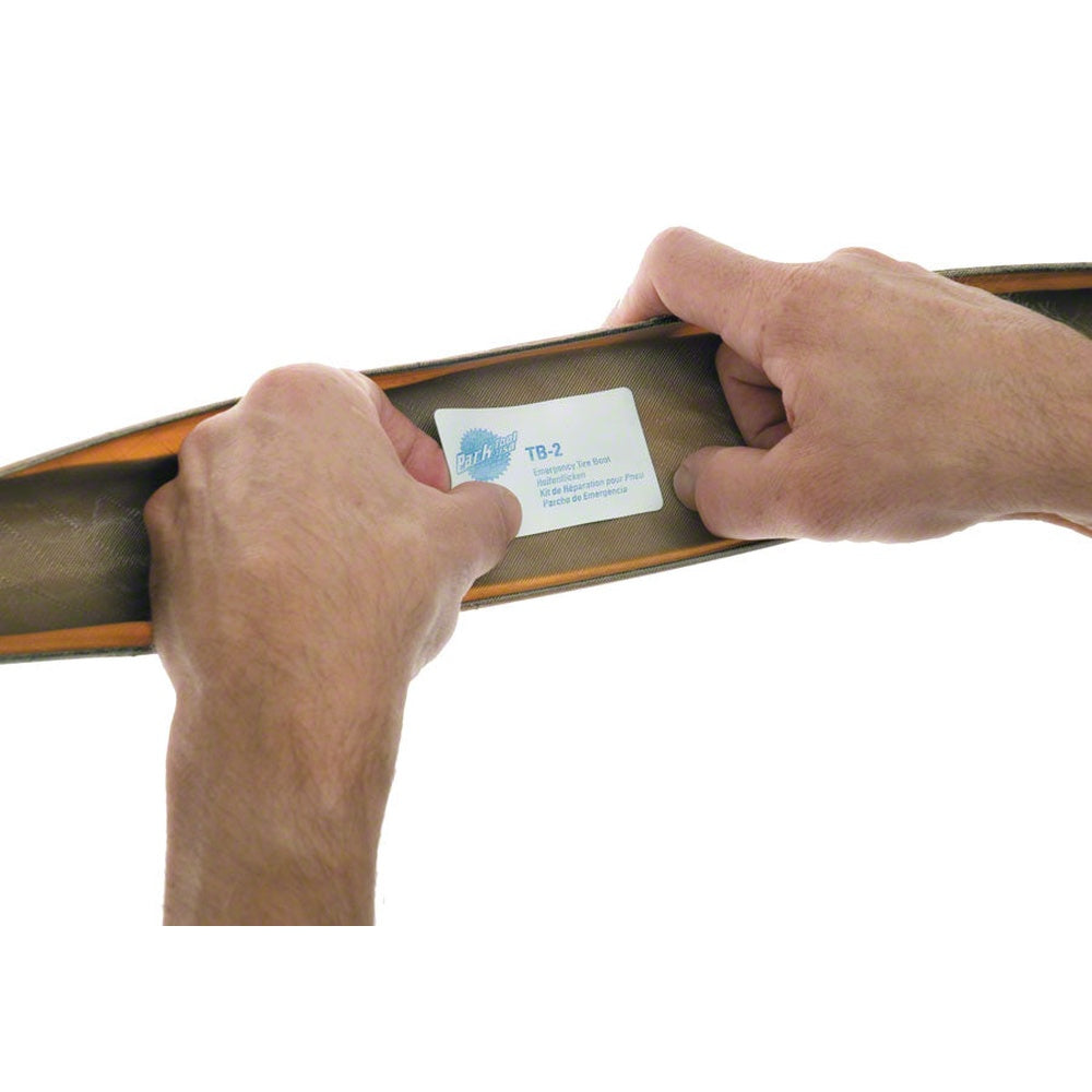 Hands demonstrating Park Tool tire boot patch on brown fabric surface