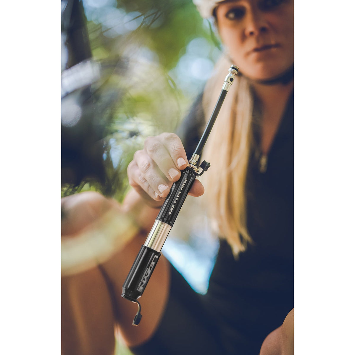 Woman cyclist holding Lezyne Pressure Drive S mini bike pump outdoors in forest