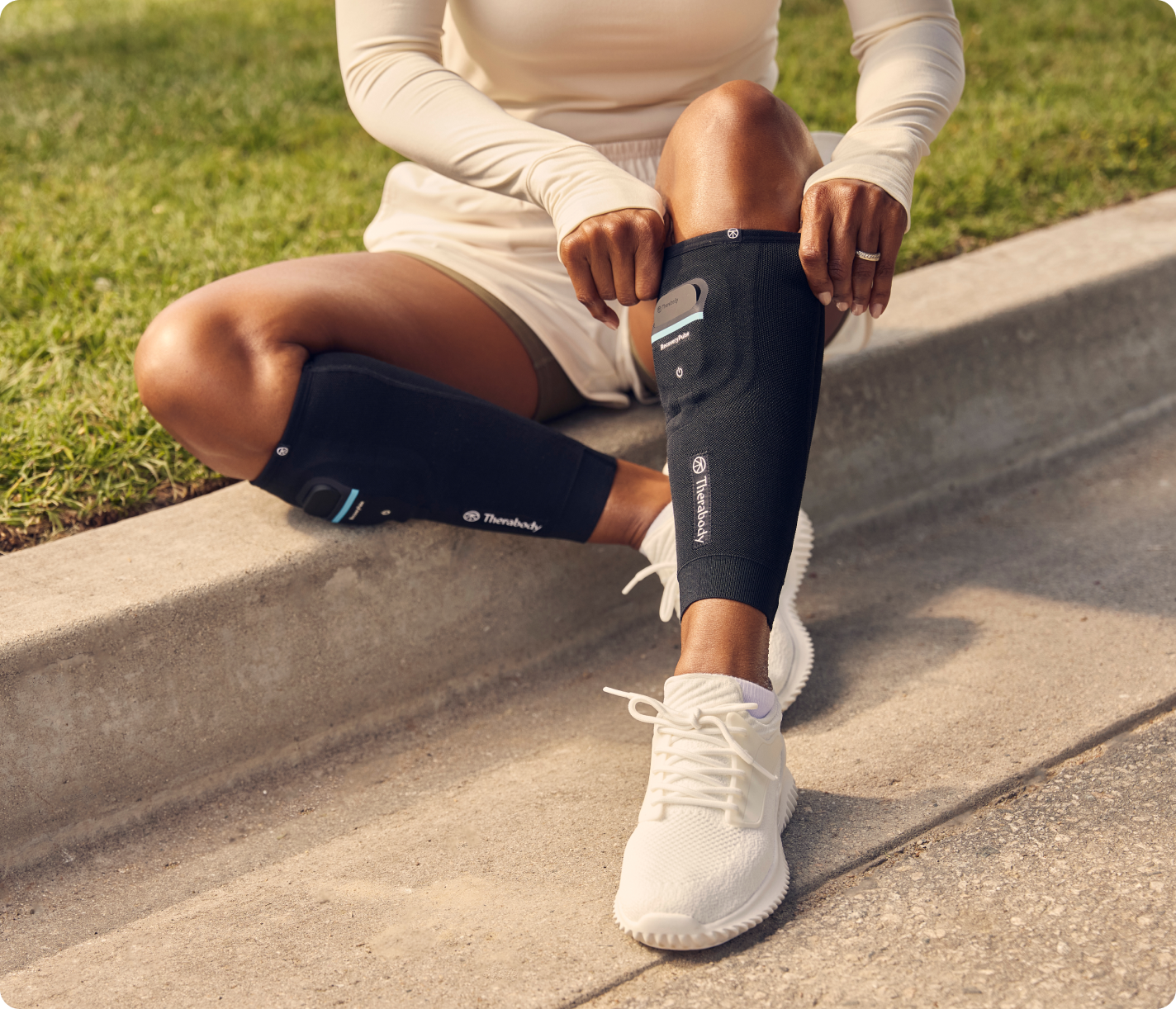 Person wearing black Therabody RecoveryPulse compression calf sleeves while sitting outdoors