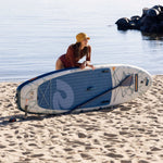 Woman in yellow hat leaning over Retrospec inflatable stand up paddle board on sandy beach
