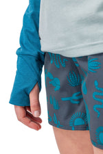 Woman wearing teal cardigan and patterned gray shorts with turquoise desert motifs