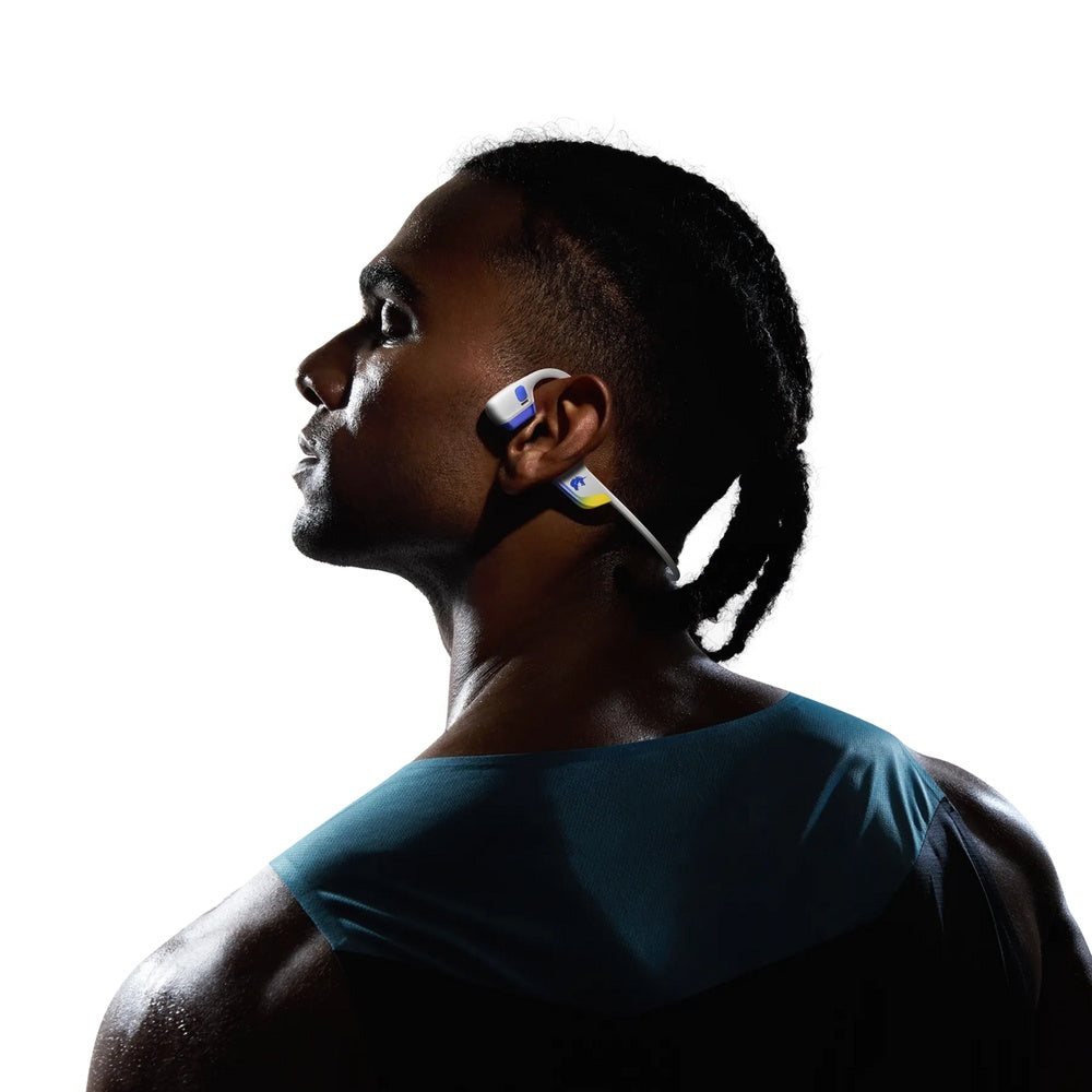 Profile view of athlete wearing white and blue Shokz bone conduction headphones