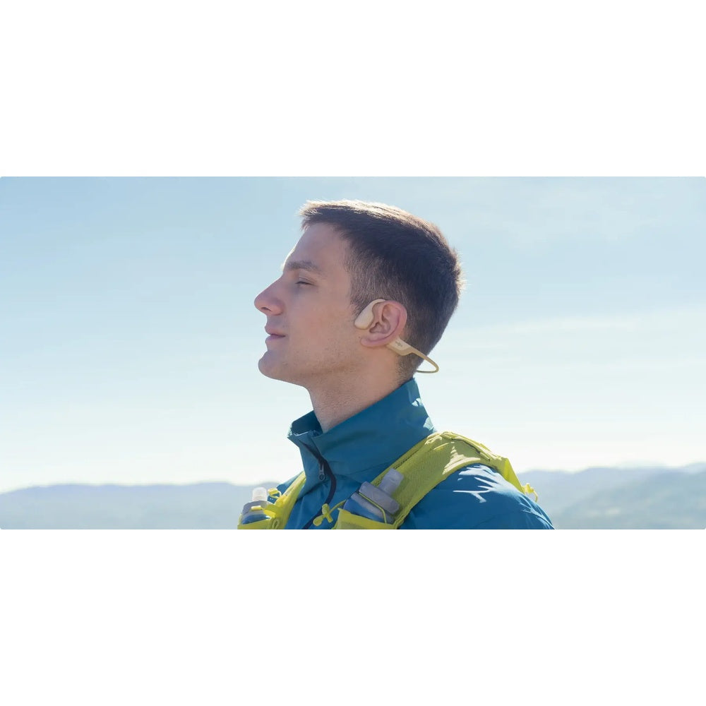 Man wearing beige Aftershokz OpenRun Pro bone conduction headphones outdoors