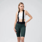 Woman wearing Gobik X dark green bib shorts with suspenders and white sports bra