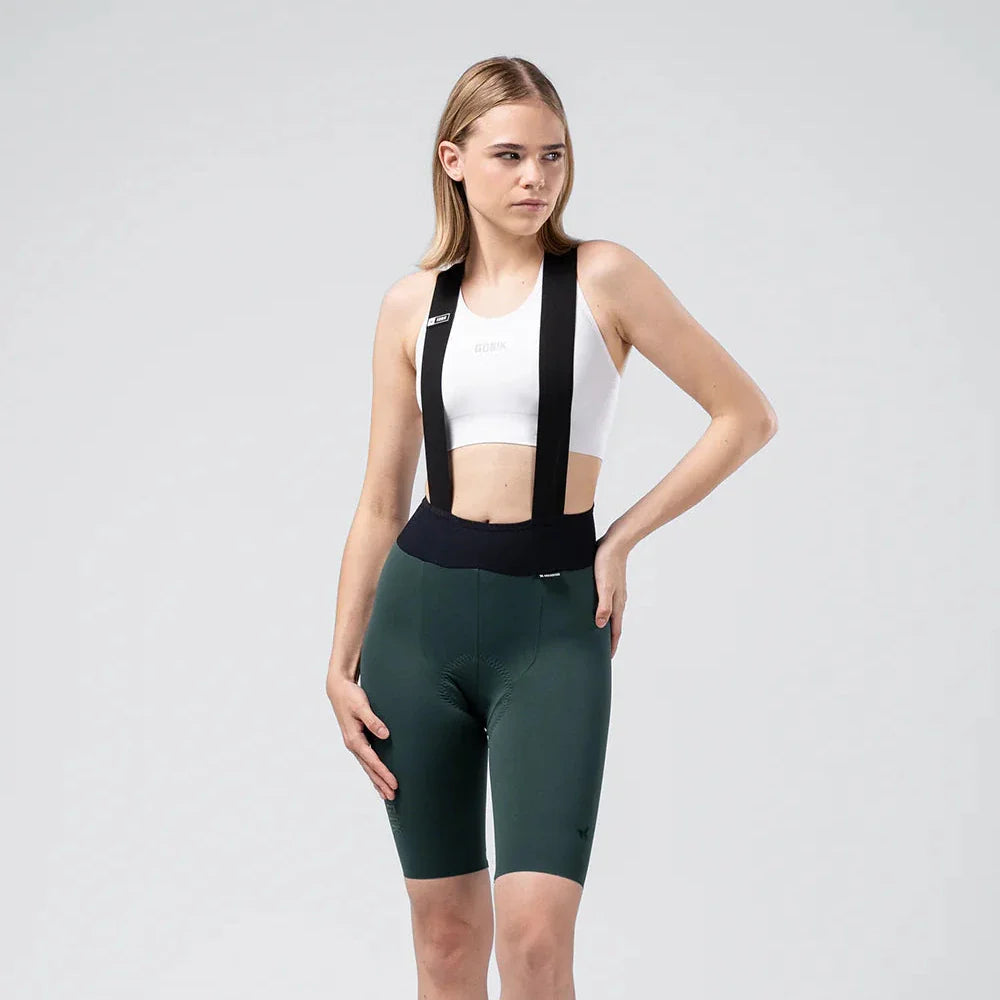 Woman wearing Gobik X bib shorts in dark green with white sports bra
