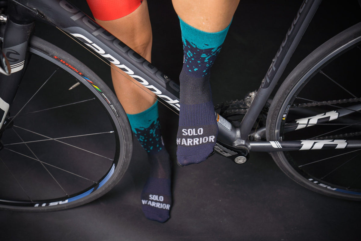 Solo Warrior cycling socks in navy blue and turquoise worn by cyclist next to road bike