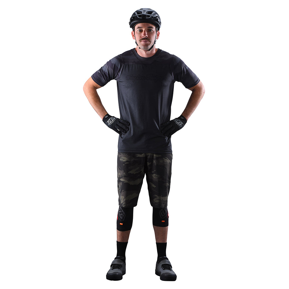 Male cyclist wearing Troy Lee Designs camo MTB shorts with knee pads and helmet