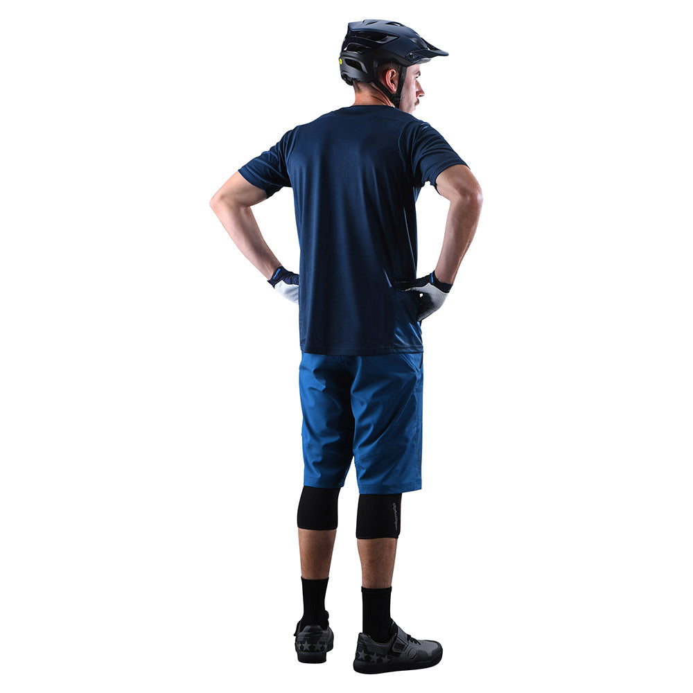 Man wearing Troy Lee Designs blue cycling shorts and navy shirt, back view