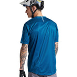 Male model wearing Troy Lee Designs Flowline Jersey in slate blue, rear view with helmet