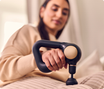 Woman holding black Therabody Theragun Sense massage gun on bed