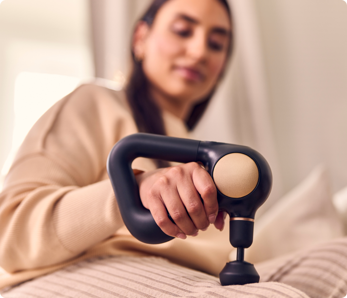 Woman holding black Therabody Theragun Sense massage gun on bed