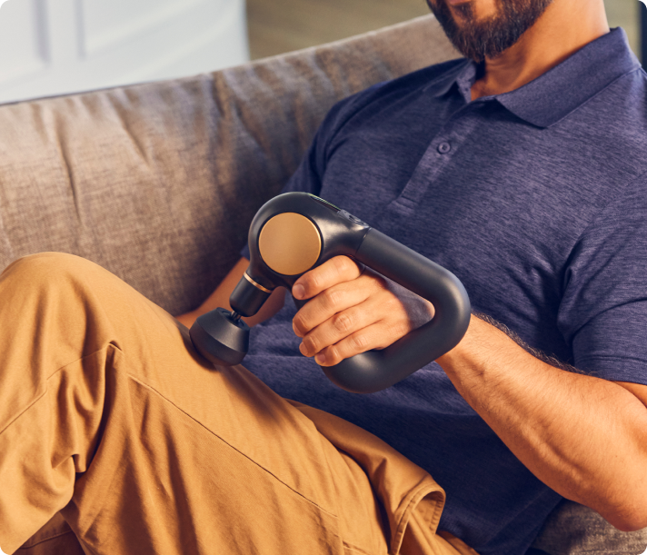 Man using black Therabody Theragun Sense percussion massager while sitting on couch