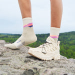 Feetures Trail Max Cushion Mini Crew socks in light gray with colorful stripes worn outdoors