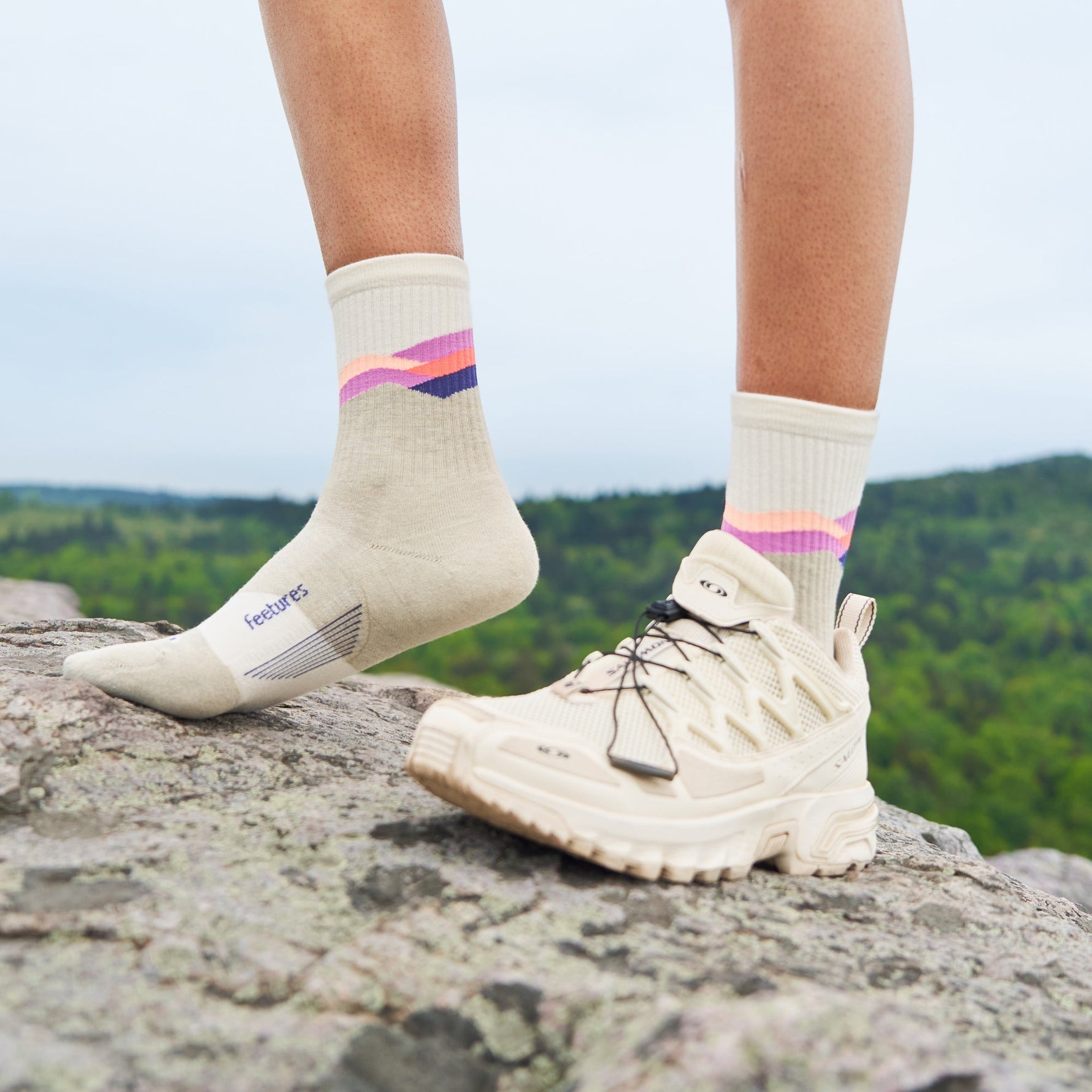 Feetures Trail Max Cushion Mini Crew socks in light gray with colorful stripes worn outdoors