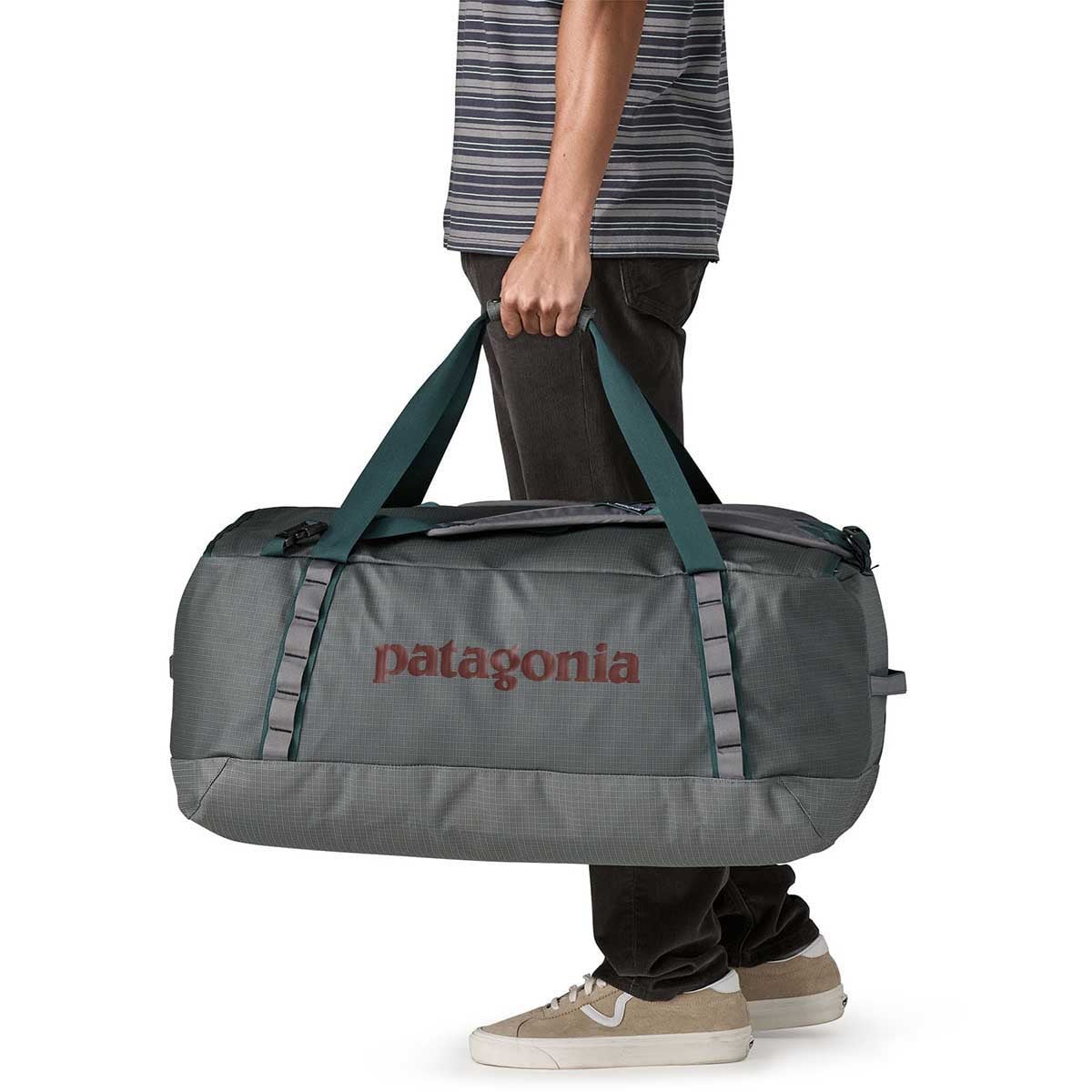 Person carrying grey Patagonia Black Hole Duffel 70L bag with teal straps