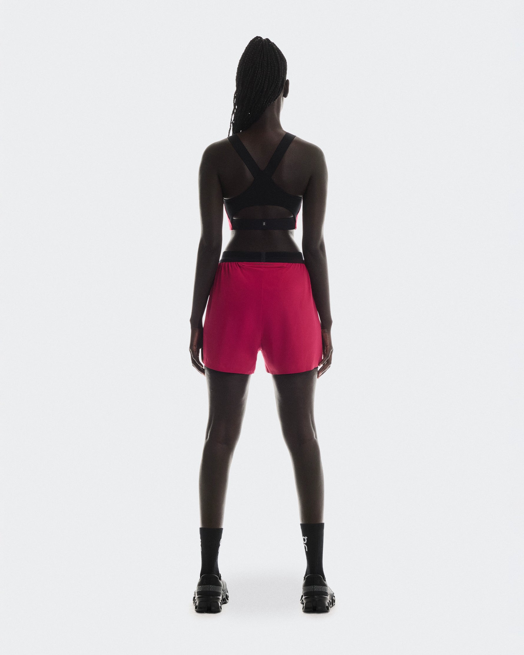 Back view of woman wearing On Performance 2/1 shorts in pink with black top
