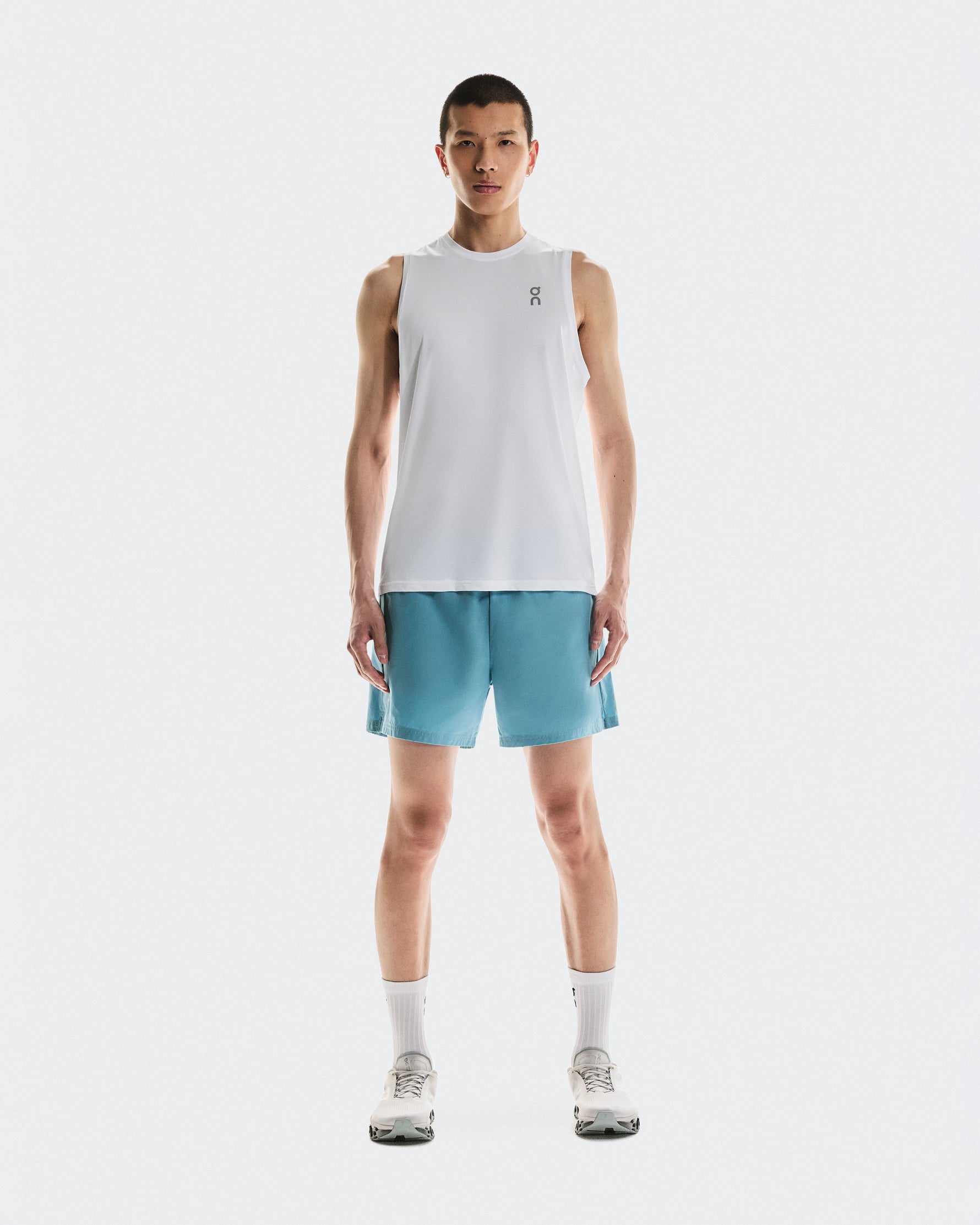 Male model wearing On 5 inch Core Shorts in Niagara blue with white tank top