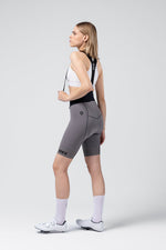 Woman wearing GOBIK gray cycling bibshorts with black straps and white sports bra