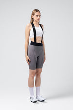Woman wearing GOBIK gray cycling bibshorts with black suspenders in studio setting