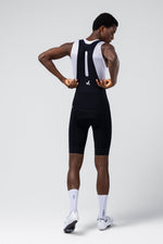 Male cyclist wearing Gobik black bib shorts with white mesh straps, rear view