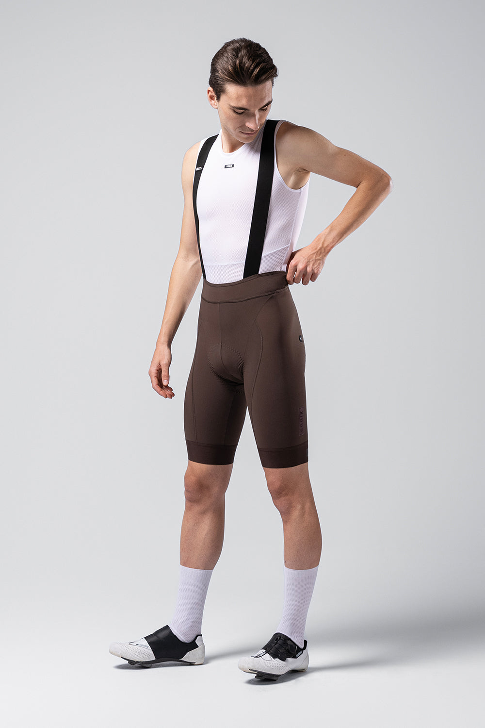 Male cyclist wearing dark brown Gobik Matt 2.0 bib shorts with white jersey