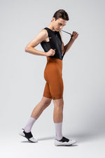 Male model wearing Gobik Matt 2.0 bib shorts in orange with black sleeveless top
