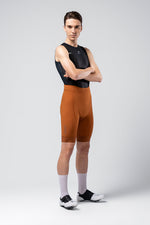 Male cyclist wearing orange Gobik Matt 2.0 bib shorts with black sleeveless top