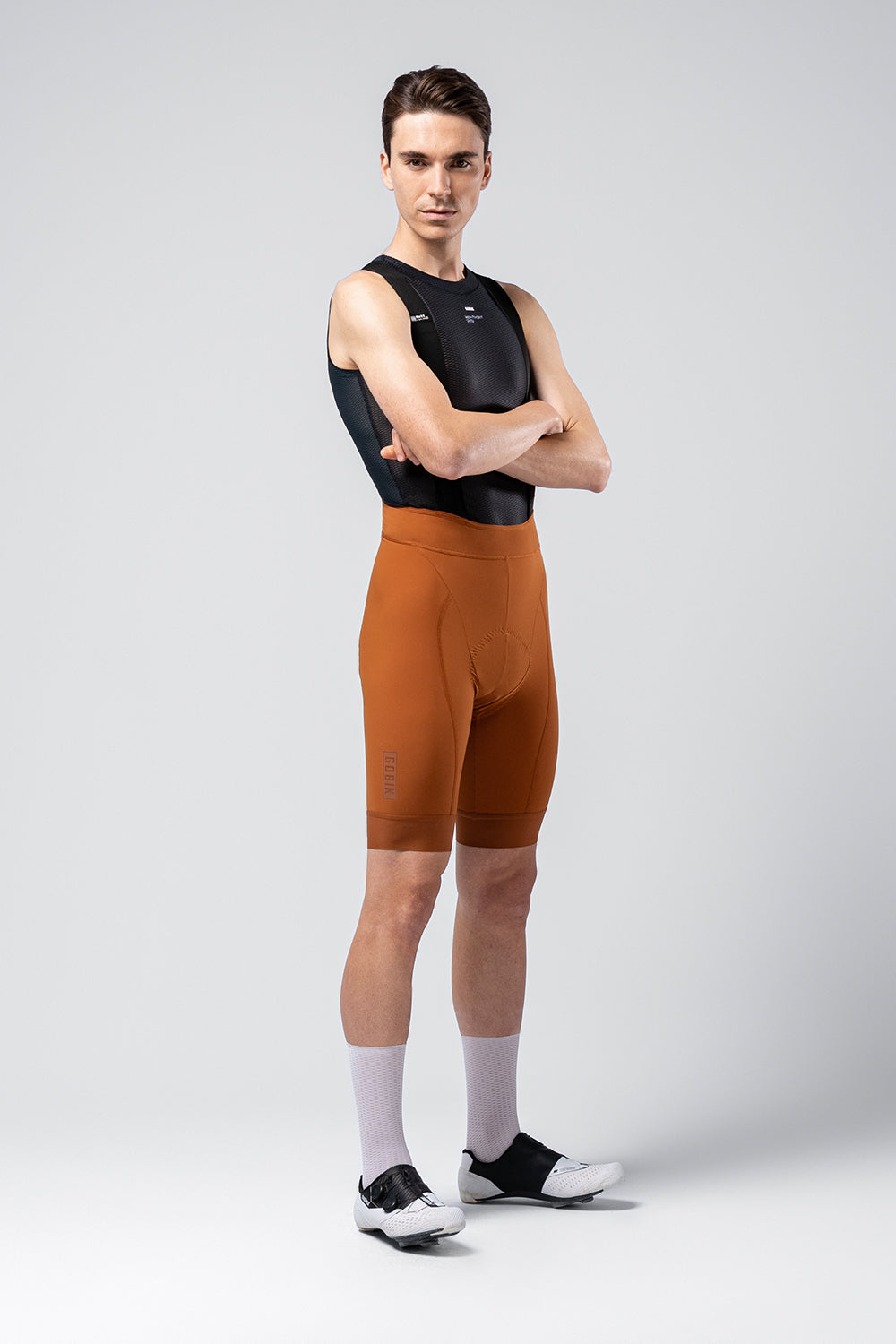Male cyclist wearing orange Gobik Matt 2.0 bib shorts with black sleeveless top