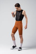 Male cyclist wearing orange Gobik Matt 2.0 bib shorts with black base layer