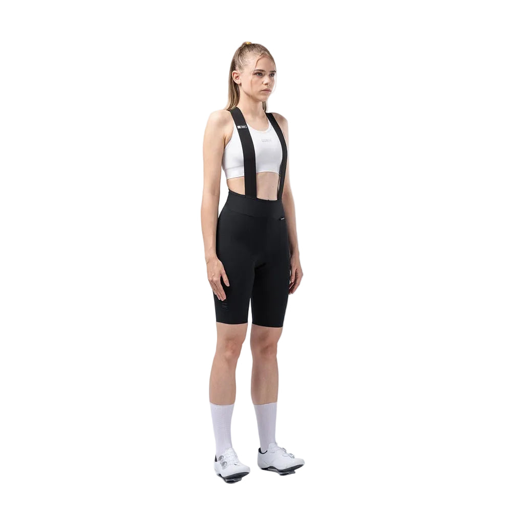 Woman wearing black Gobik X bib shorts with white sports bra in studio setting