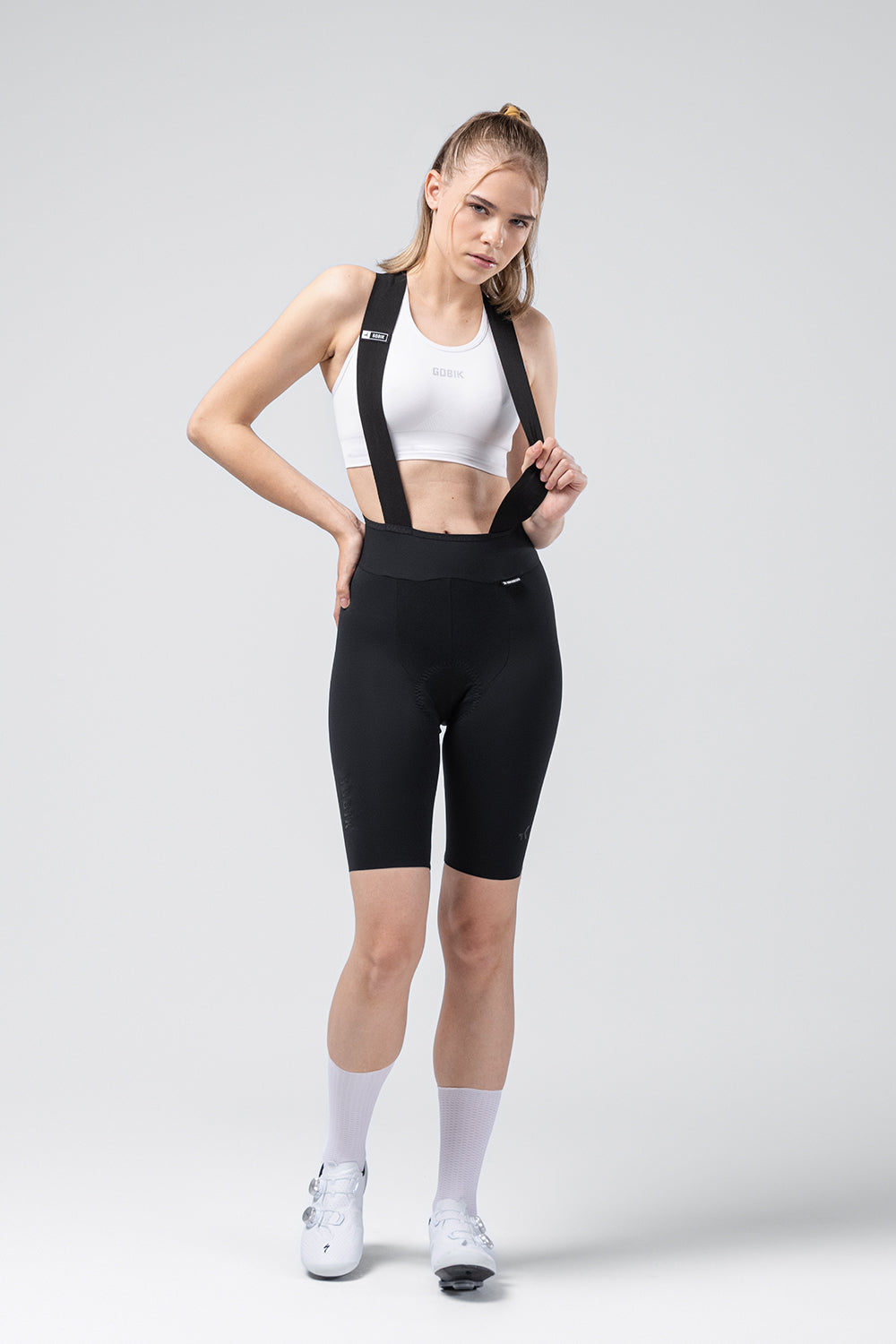 Woman wearing black Gobik X bib shorts with white sports bra and white socks